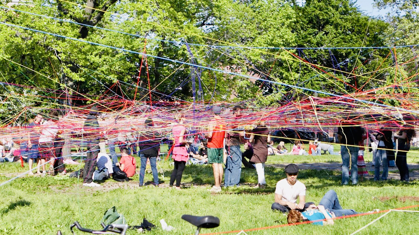 Crowds moving through a sprawling rainbow string installation by Jasmine
