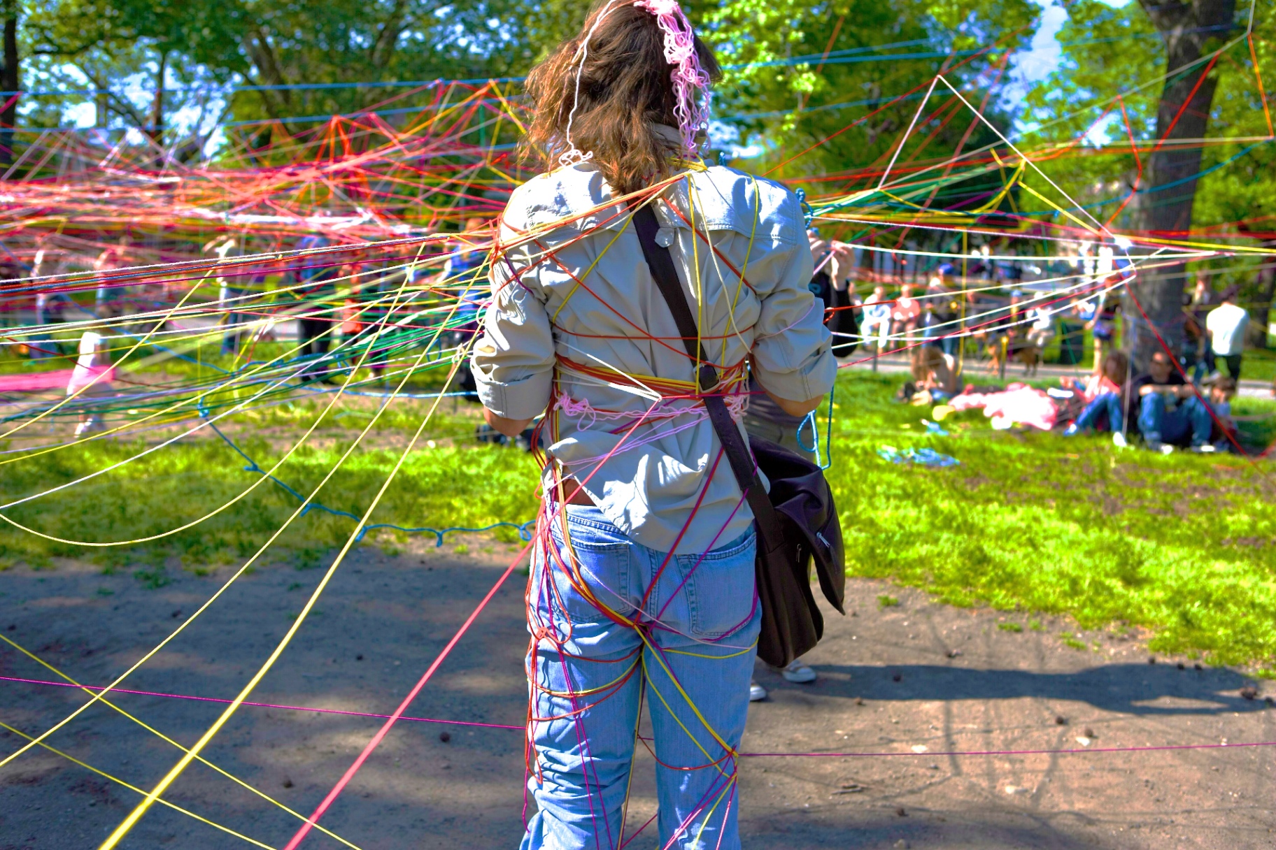 A visitor seen from behind, wrapped to the ankles in the colored strands of a rainbow string web
