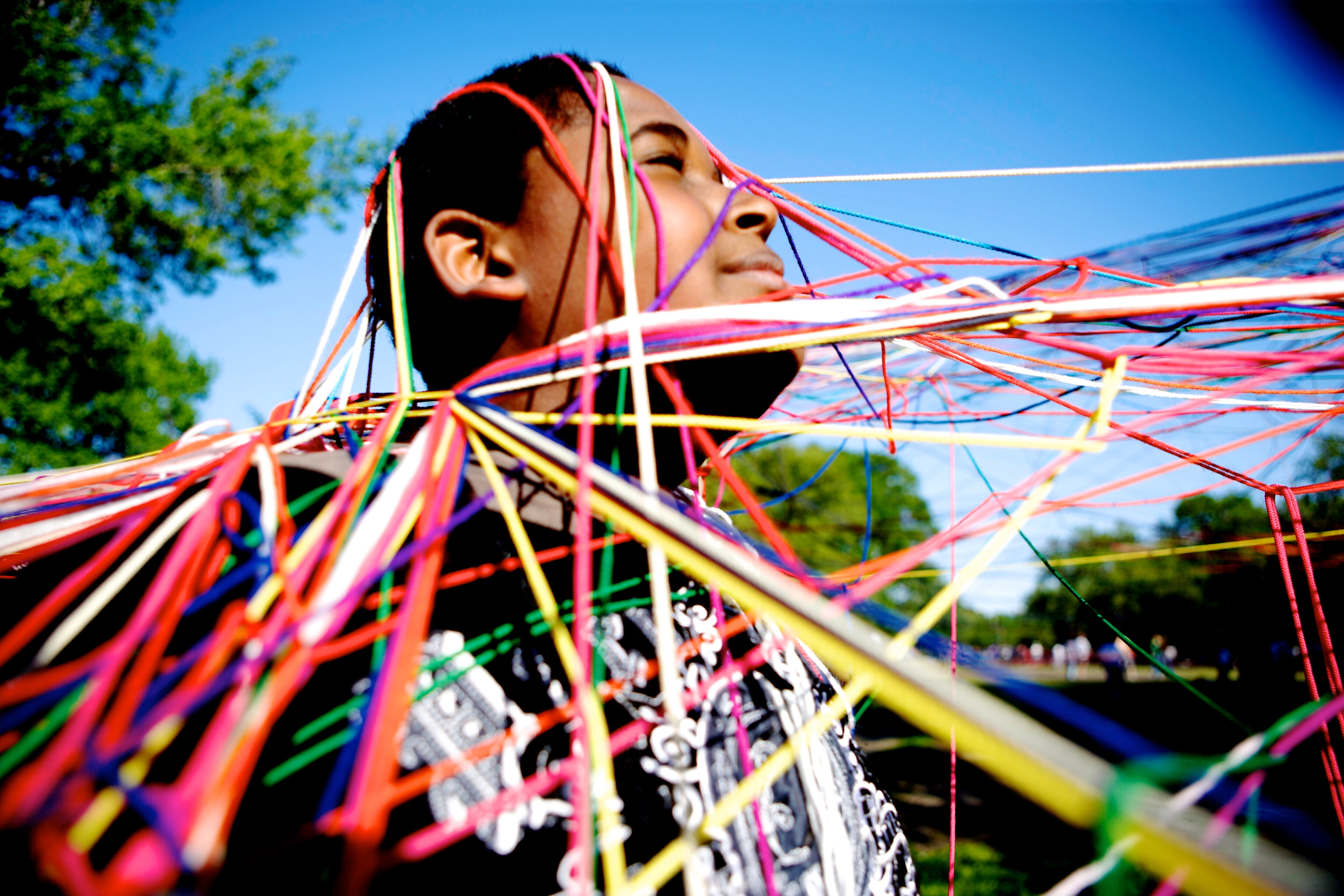 A child stands in the sun wrapped in a web of rainbow-colored strings